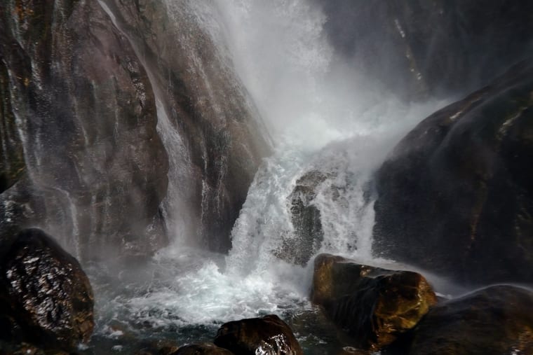 A waterfall breaking white over dark wet boulders, spray hanging in the air around it